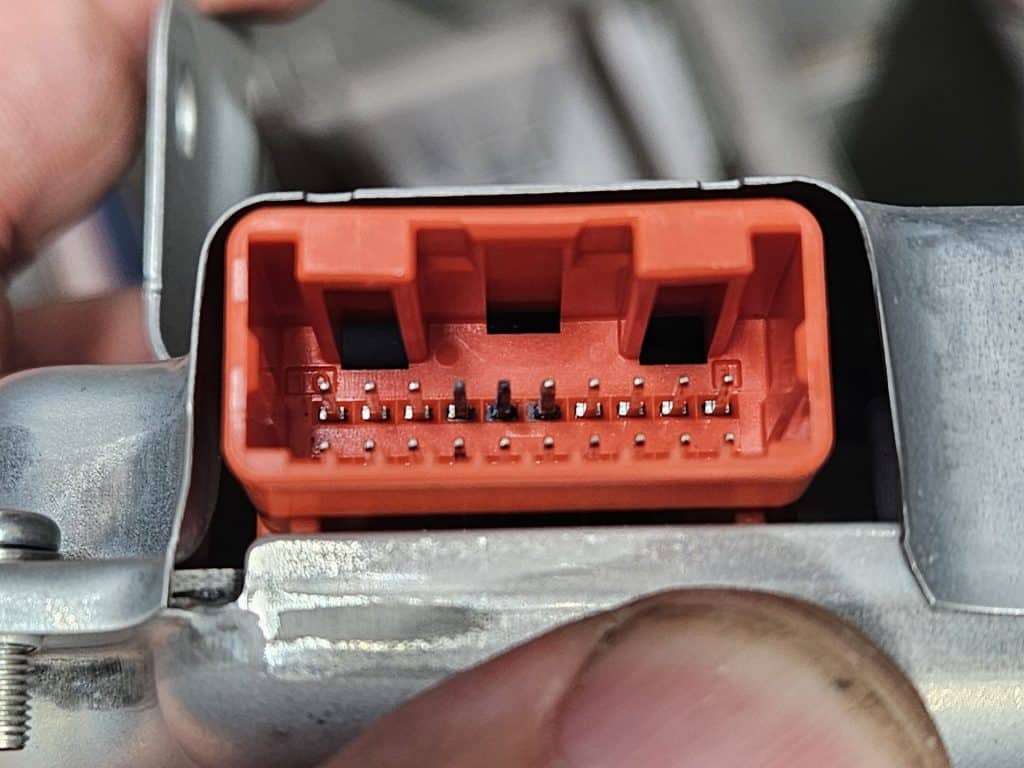 An image of an orange connector with 20 terminals. Three of the terminals are blackened with oxidation the other 17 are clean and shiny.