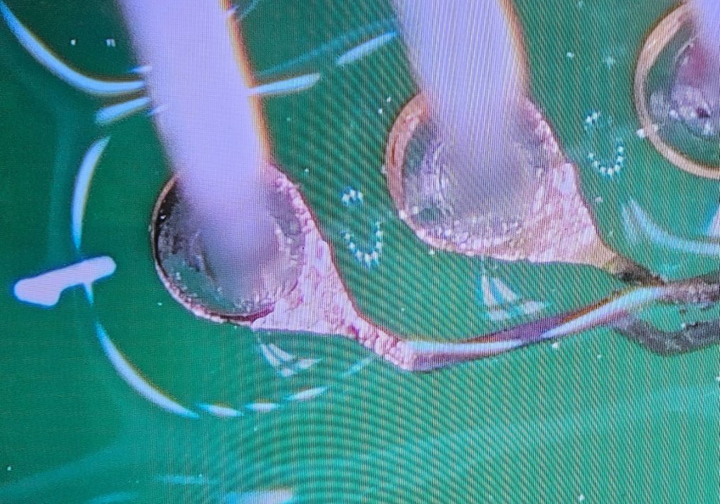 A very close up image of through hole terminals going into a circuit board. The coating on the pads has been removed to expose copper.