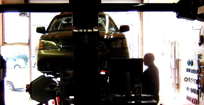 backlit image of car and mechanic performing wheel alignment