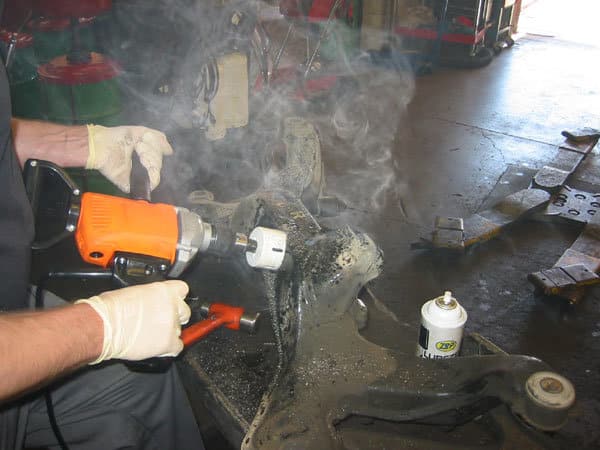 a mechanic cutting through metal with a hole saw with clouds of oil smoke