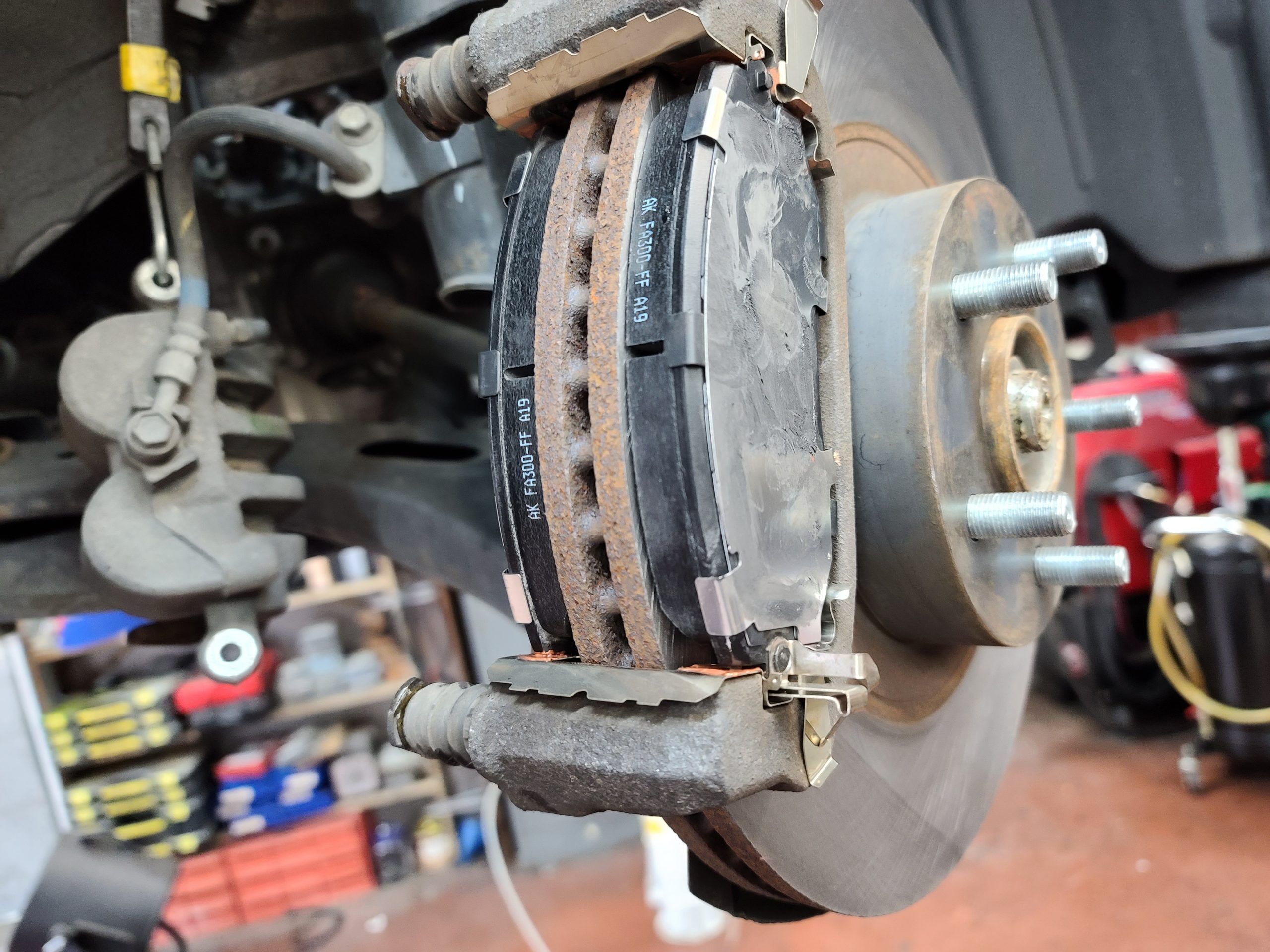 A half-complete brake repair. The caliper is suspended with a bungie to prevent strain on the brake hose. Art's Automotive auto repair shop in Berkeley sits in the background.