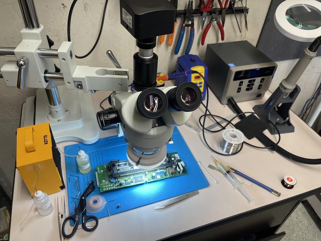 An electronics repair station with a microscope, soldering station, hot air station, fume extractor, and Prius combination meter circuit board being repaired