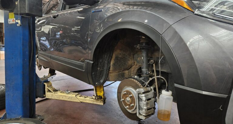 A Honda CR-V hybrid on the rack with a brake bleeder attached.