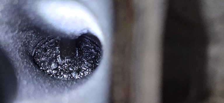 A close up of a dirty intake valve covered with carbon deposits.