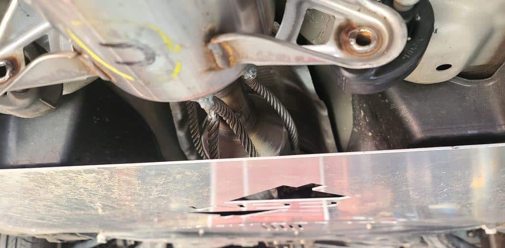 The underside of a Toyota Prius with two different catalytic converter anti-theft devices installed. A shield covering the converter and cables welded to the converter and exhaust manifold.