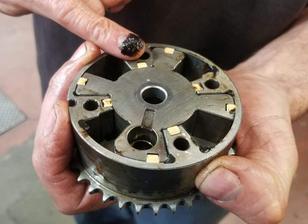 A mechanic scooping black goop from a disassembled Prius VVT sprocket.