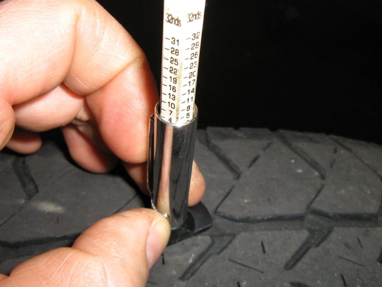 A mechanic checking tire tread depth with a gauge.